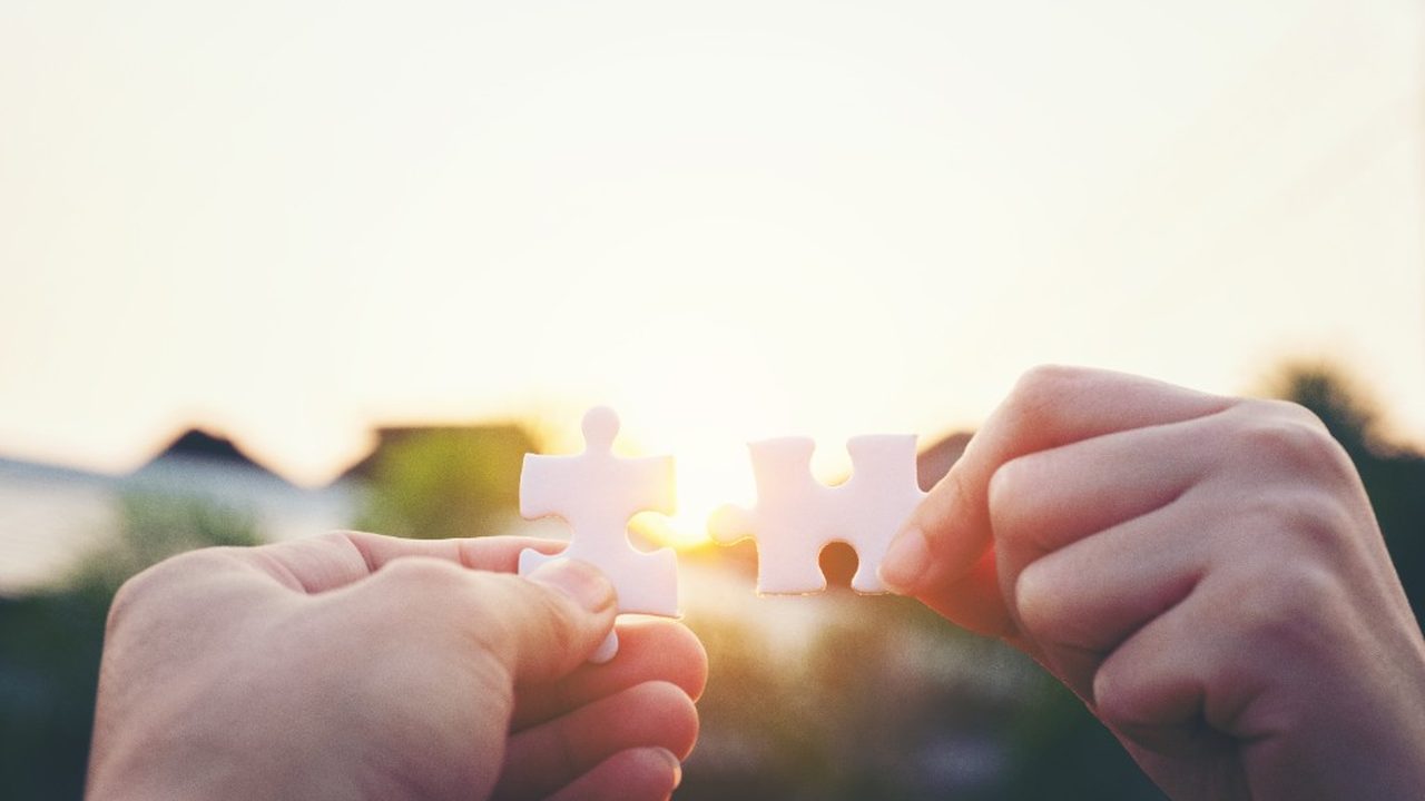 Two hands joining puzzle pieces in warm sunrise light