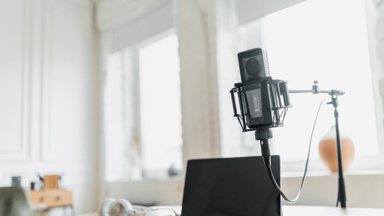 A studio microphone, laptop, and headphones on a bright desk